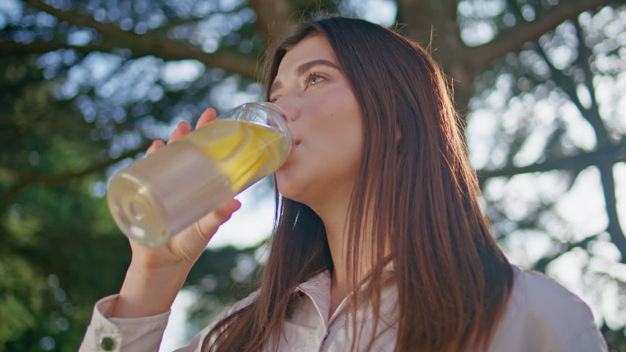 여름 공원에서 물을 보충하는 여행자. 레몬 음료를 마시는 여성 클로즈업