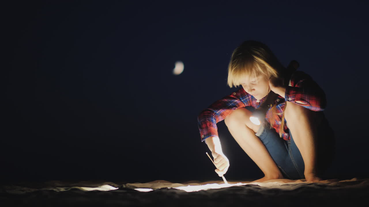 una chica con una linterna en la mano está buscando algo en la playa en la investigación oscura y