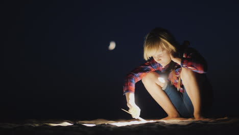 a girl with a flashlight in her hand is looking for something on the beach in the dark research and