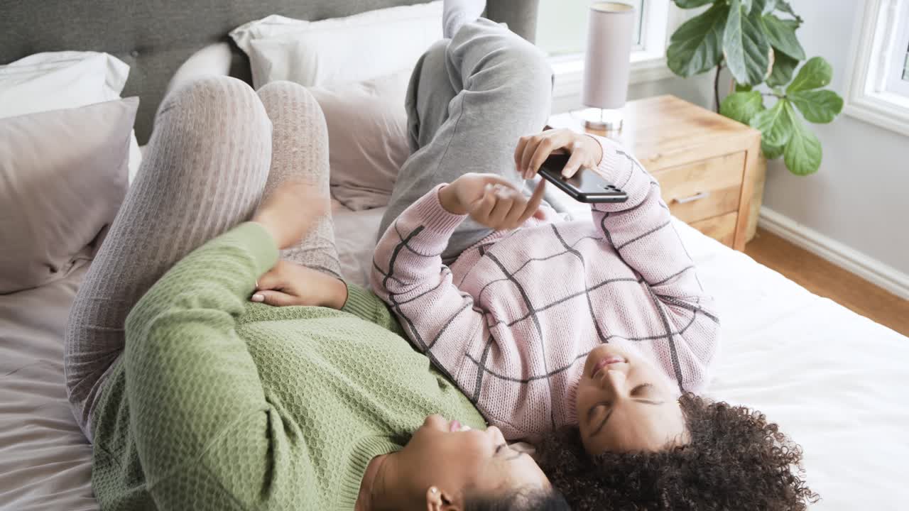 Glade unge kvinder, der ligger på sengen og deler indhold på smartphone