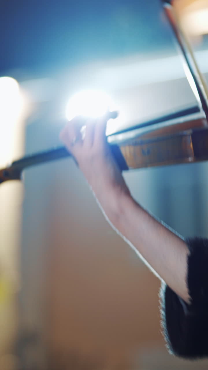 A creative girl in a black coat is playing the violin a romantic melody on the background of light from an evening lantern in the city. Close-up Vertical video