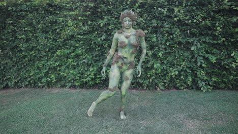 Wide-shot-of-a-female-model-wearing-green-bodypaint-dancing-slowly-in-nature,-in-the-style-of-nature-inspired-forms