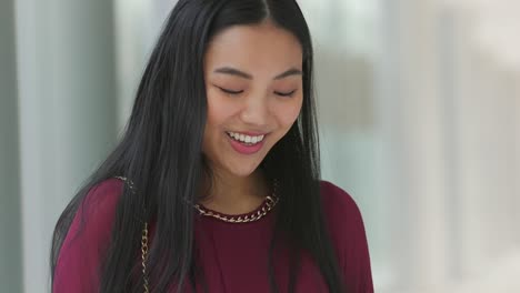 Close-up-of-Asian-woman-looking-at-her-phone-and-then-smiling-and-laughing-then-looking-back-down