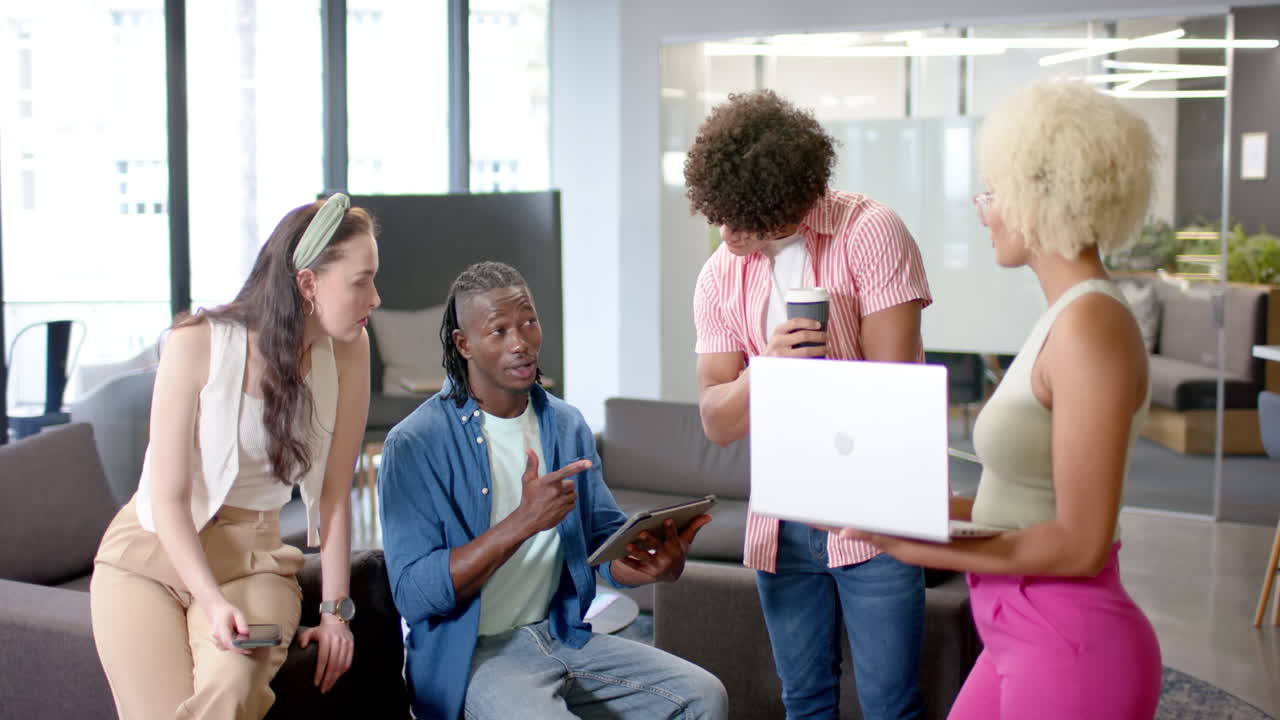 Discussing project, diverse team collaborating in office using tablet, smartphone, and laptop