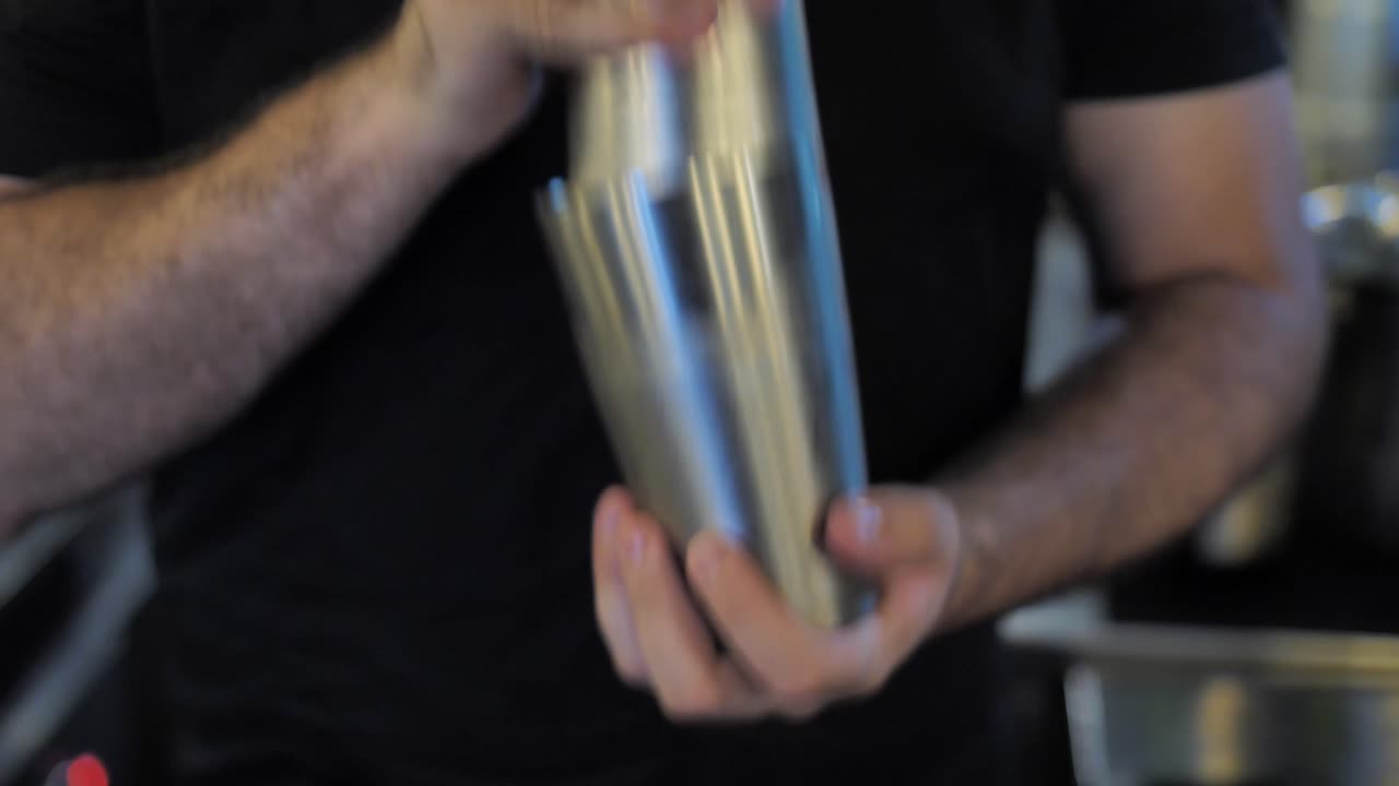 camarero irreconocible agitando un cóctel en una coctelera de acero en el pub, de cerca