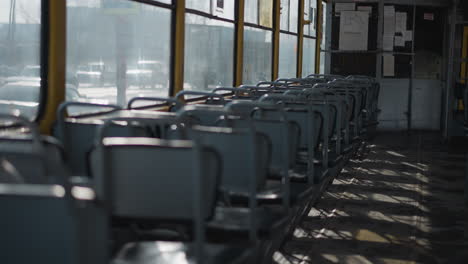 nearly empty train interior shows rows of blue seats in winter light while single passenger rides at back, city cars glide past windows, long shadows stripe worn floor, calm transit mood