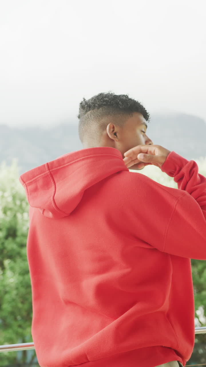 Video verticale di un ragazzo adolescente afroamericano felice che indossa una felpa con cappuccio rossa, spazio per il testo.