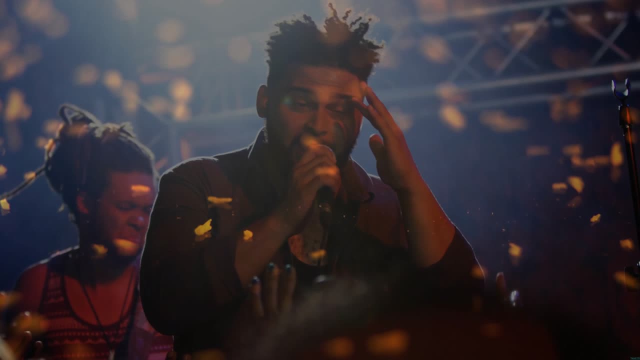 Lead singer raising mic singing to move music crowd at concert, golden confetti drifting over faces