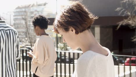 Side-view-of-young-citizens-walking-on-street-with-phones