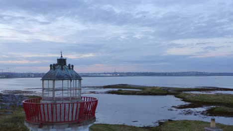 Impresionantes-Vistas-Aéreas-Del-Faro-De-Mutton-Island-Y-La-Planta-De-Tratamiento-De-Aguas-Residuales-En-Galway,-Irlanda-El-Dron-Se-Mueve-Hacia-Atrás-Y-Hacia-Arriba,-Revelando-La-Hermosa-Costa