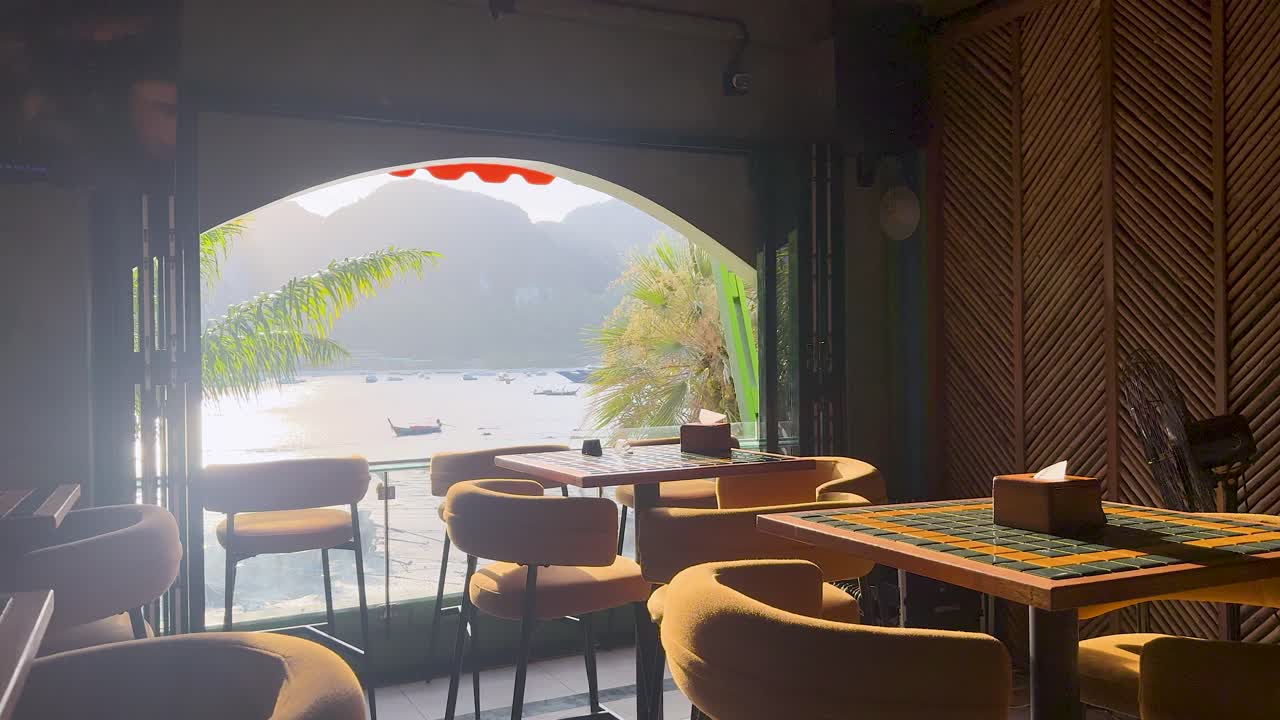 Static wide shot of an empty tropical restaurant interior with bright sunlight over the bay