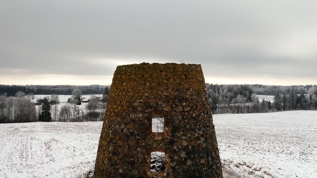 Abandoned windmill ruins in the middle of a field. Winter drone shot with snow covered ground and forest in the background.