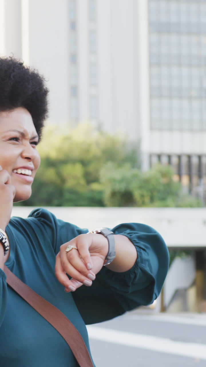 mujer biracial feliz de talla plus hablando en su teléfono inteligente y revisando su reloj inteligente
