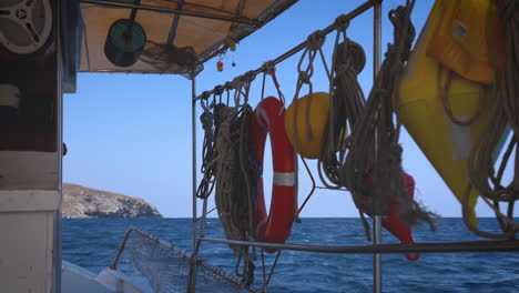 nautical ropes and life-saving equipment hang from a boat railing with the sea and distant hills in the background