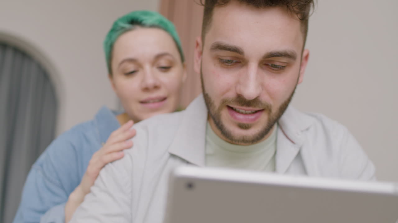 вид крупным планом молодого человека, использующего планшет, в то время как его девушка обнимает его со спины