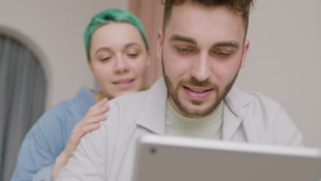 close up view of young man using a tablet while his girlfriend hugging him from his back