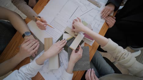 a team of architects and designers gather around a table, examining building plans and discussing various material samples for a construction project