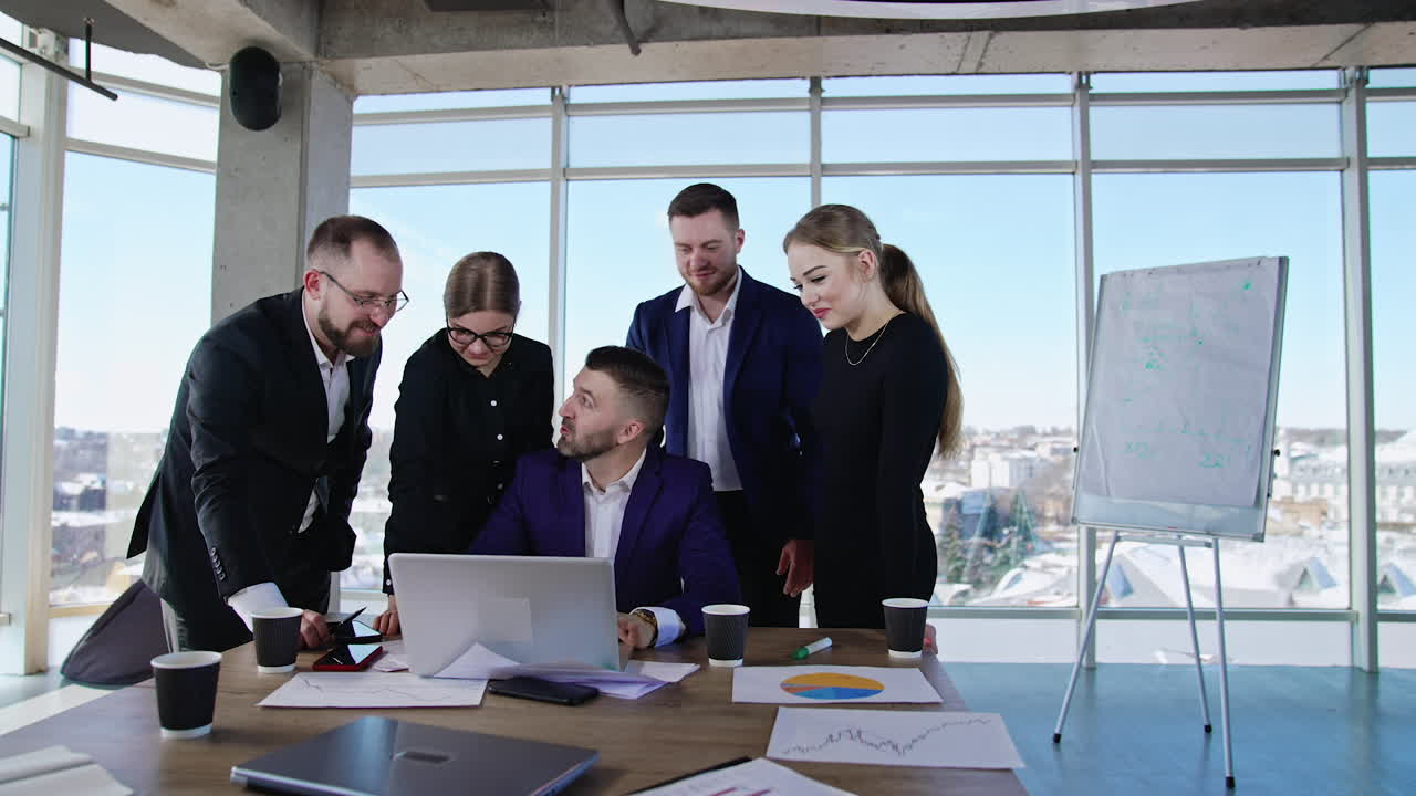 Positive young workmates team brainstorming in office. Man in the centre typing on the computer and smiling. Cityscape at backdrop.