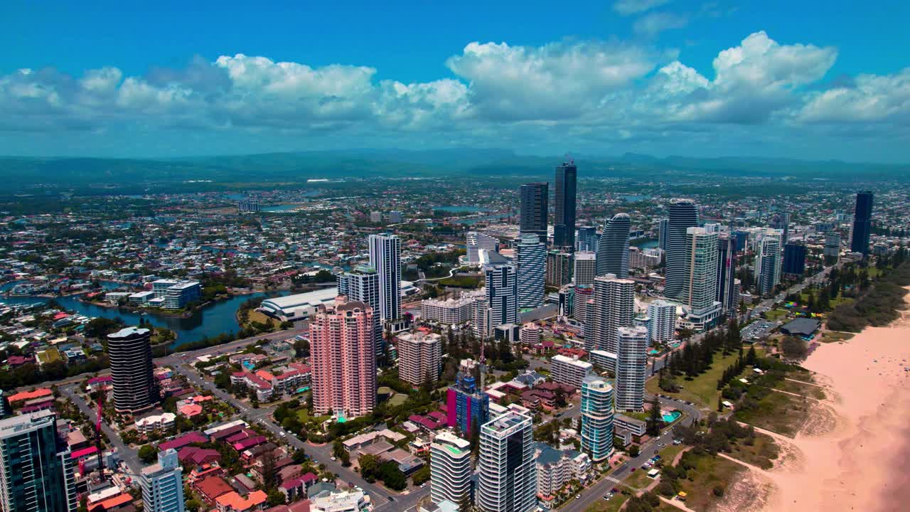 Góc nhìn từ drone trên cao của Broadbeach thuộc Gold Coast, Queensland, Úc, cho thấy các tòa nhà cao tầng ven biển, bờ cát, các tuyến đường thủy nội địa và bầu trời đầy mây ấn tượng.