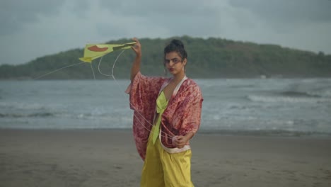 Slow-motion-shot-of-a-woman-in-a-red-cardigan-and-golden-pants-holding-a-yellow-kite-on-a-windy-beach