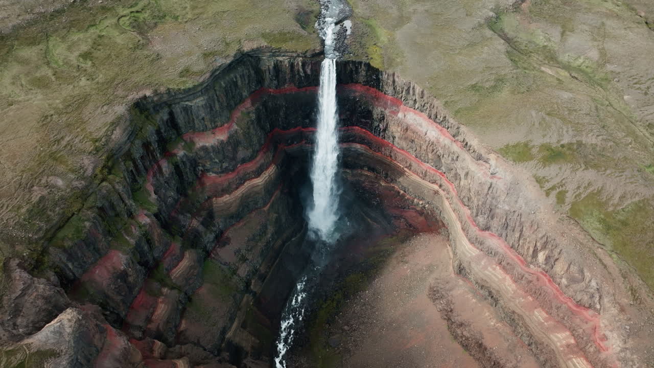 tomada aérea de un dron de la cascada de hengifoss en movimiento, islandia, día soleado, hierba verde, arcilla roja