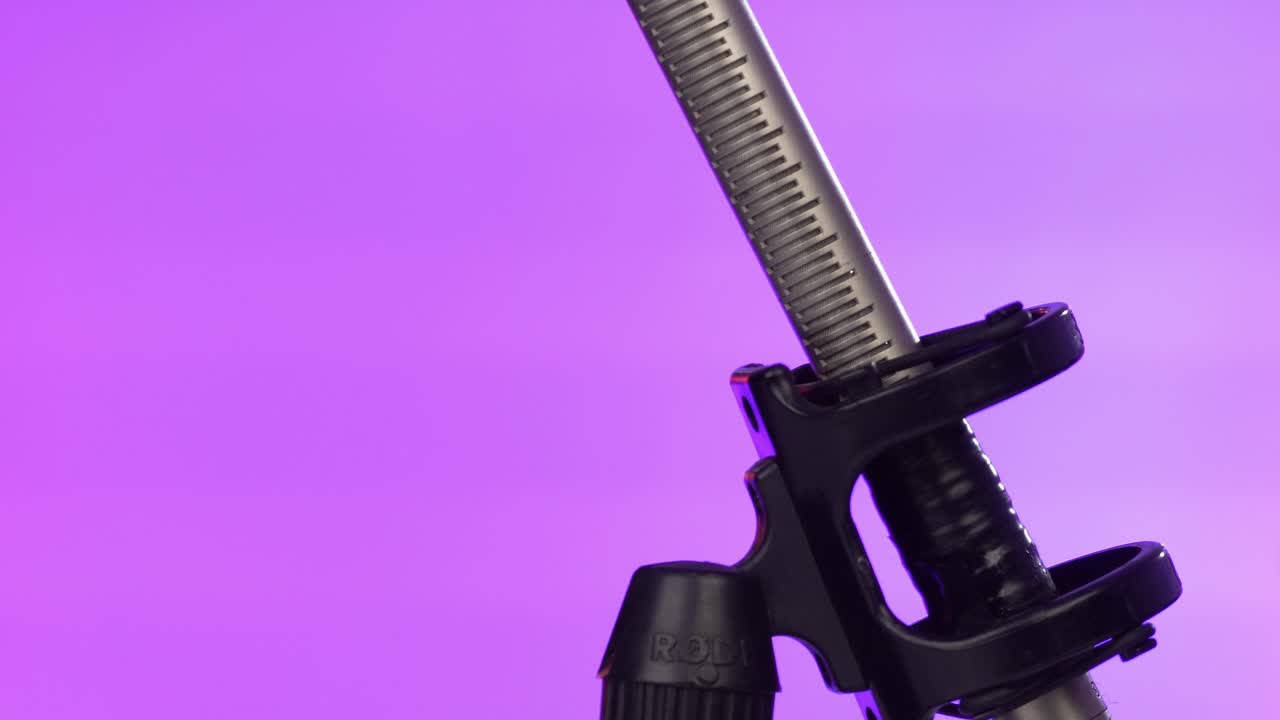 Macro shot of a metallic microphone boom rotating slowly against a vibrant purple background with studio lighting
