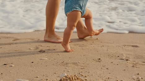 mother is support her child to do the first steps on beach sand in summer.