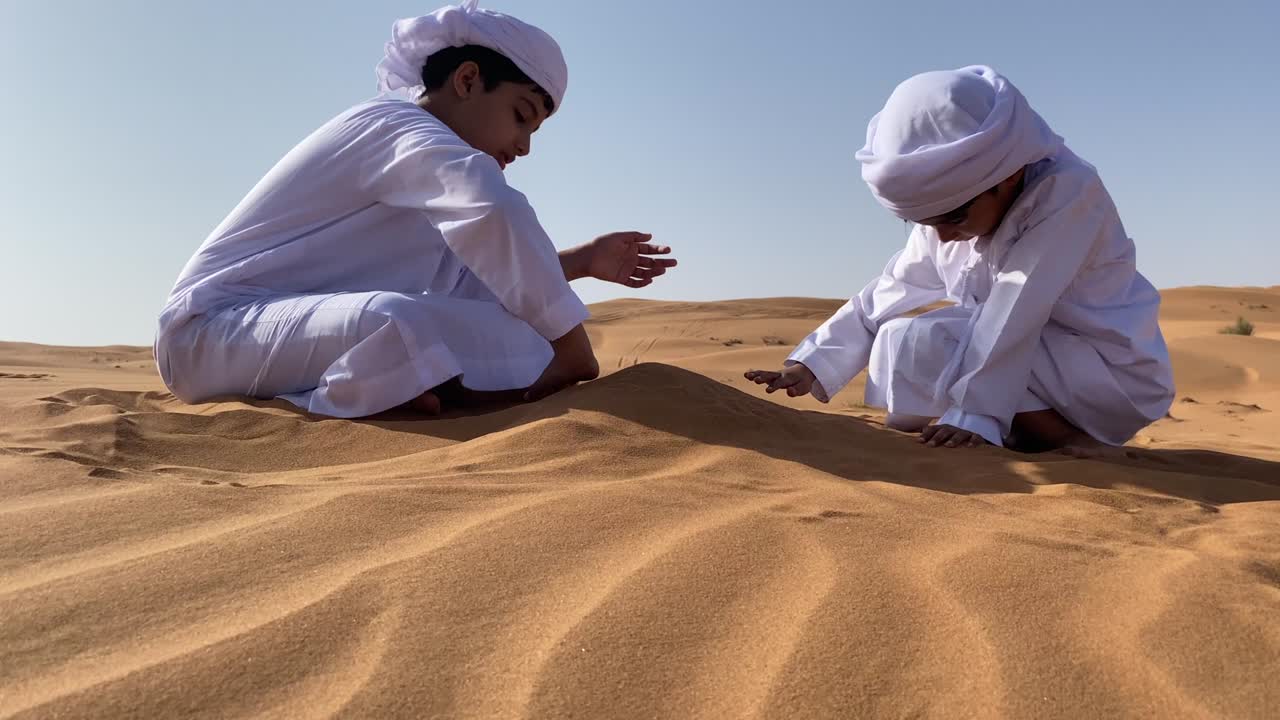 Two Emarati children playing with sand in the desert