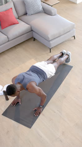 un hombre afroamericano concentrado haciendo flexiones en una sala de estar soleada, en cámara lenta.