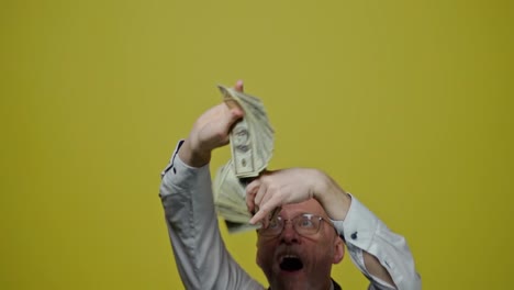 good-looking joyful man with money on yellow background. satisfied modern gray-bearded grandfather posing on camera with many dollar bills. slow motion.