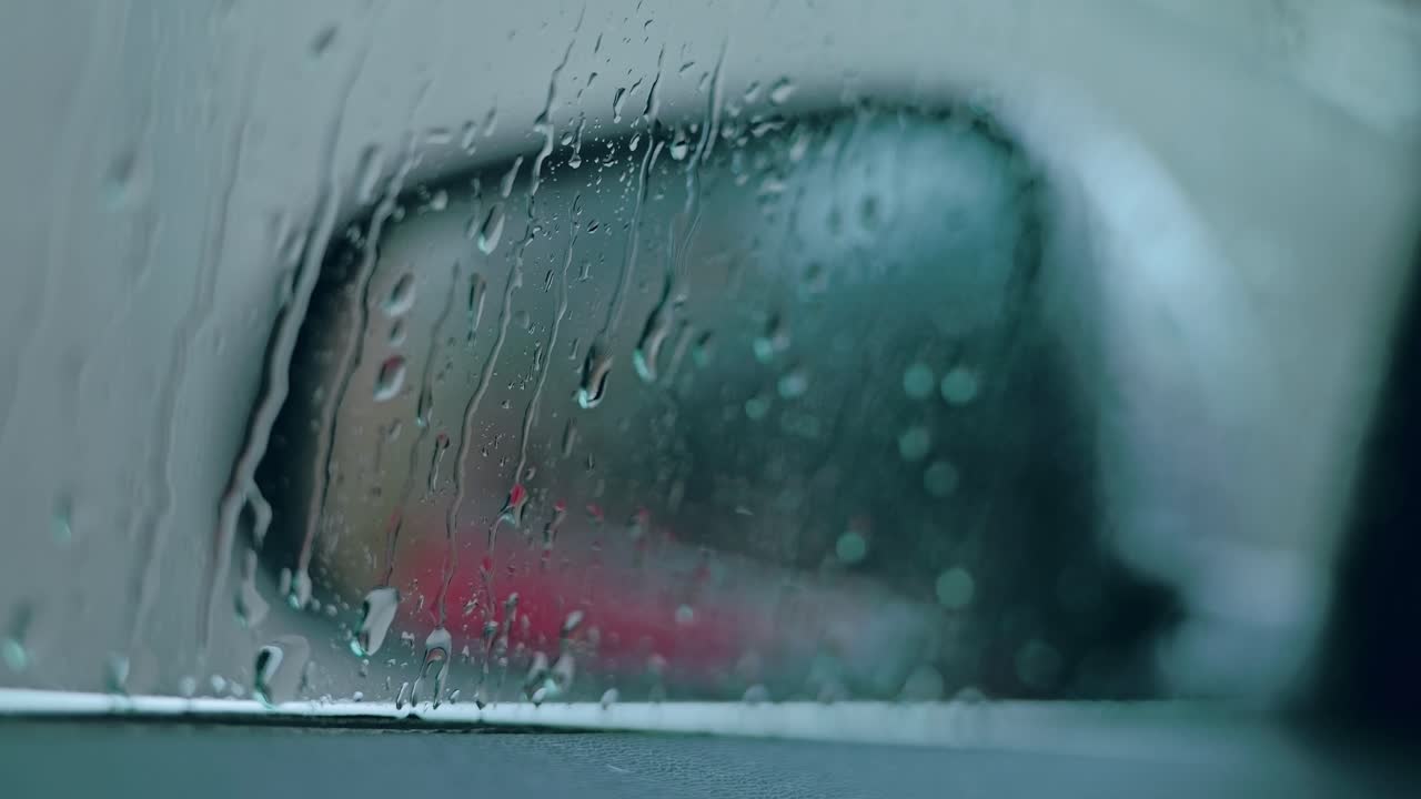 Raindrops slide down car window blurring mirror view as metaphor for insecurity
