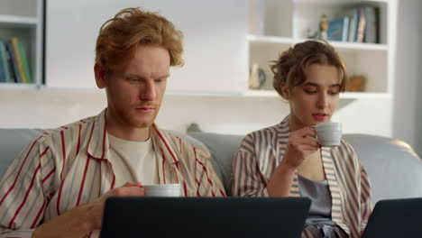 working couple drinking coffee at home office closeup. freelancers look laptops