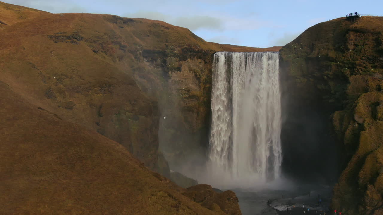 drone aéreo cinematográfico cascada de skogafoss islandia pan hacia abajo movimiento con pájaros, arco iris, niebla y nubes de luz solar de tarde