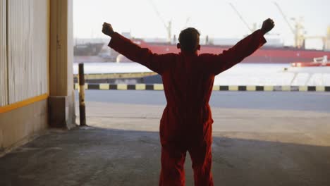 silueta de un trabajador en uniforme naranja caminando por el almacén del puerto junto al mar durante su descanso y levantando las manos