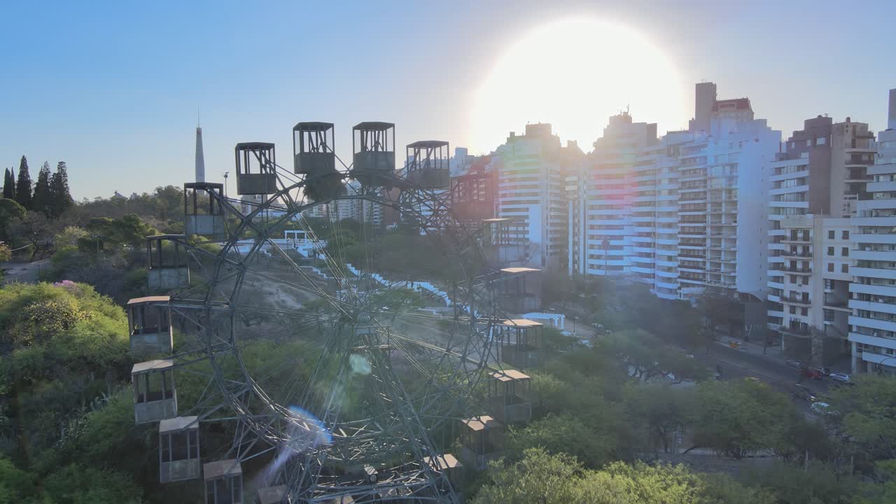 드론 비행 소박한 페리 휠은 배경에 태양이 빛나는 계단 전망대 플랫폼과 측면에 건물이 줄지어 있고 포에타 레오폴도 루곤스 애비뉴에서 교통 교차로를 보여줍니다.