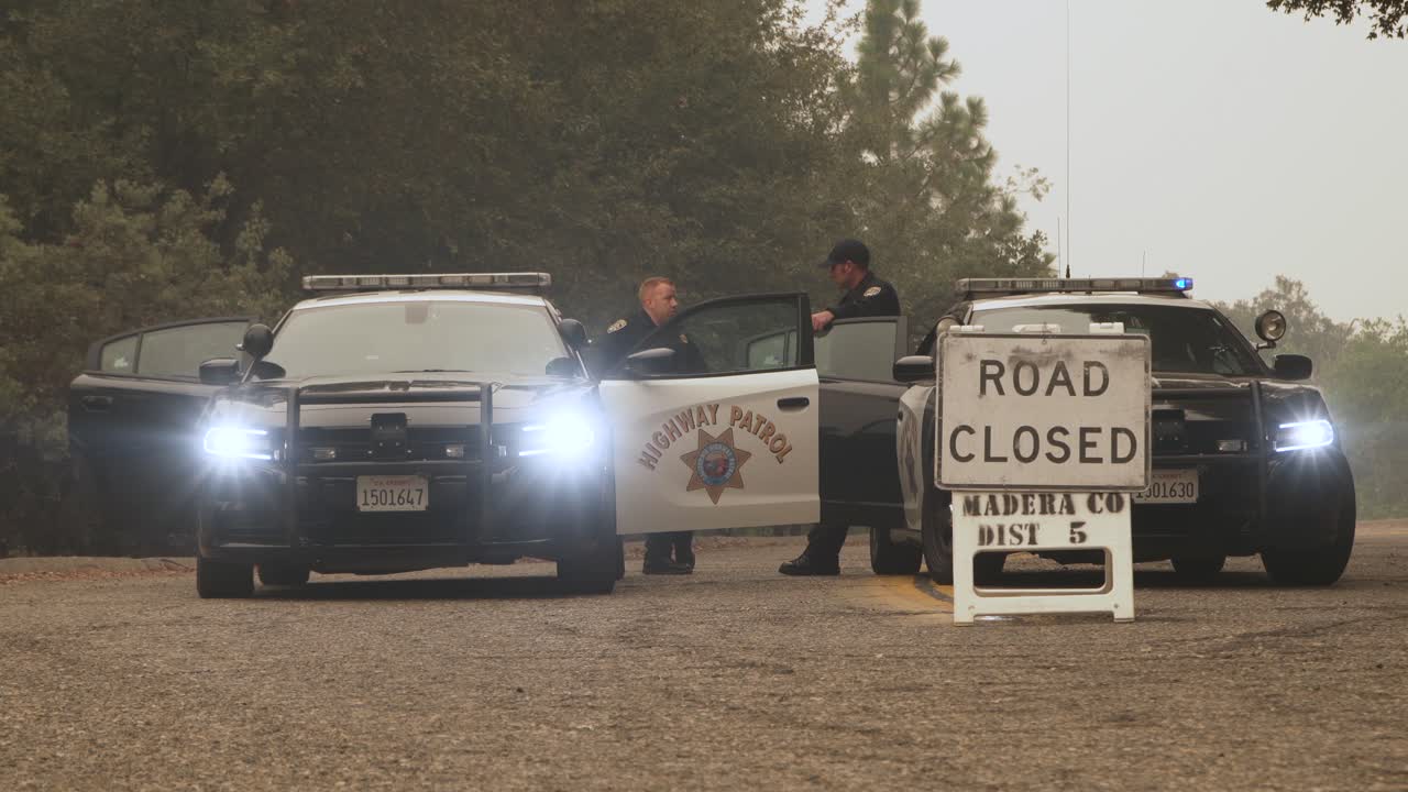 Police cars, lights flashing, block road as officers stand by, Creek fire, California