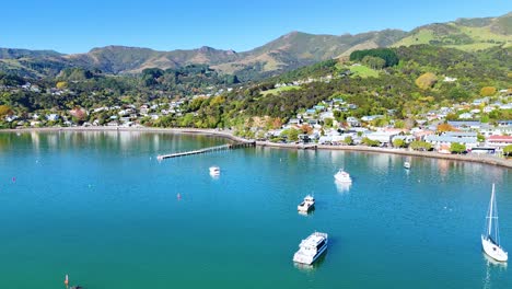aerial footage captures boats and lush hills surrounding akaroa harbour under clear skies, showcasing serene coastal beauty