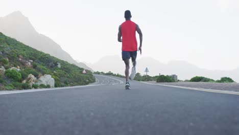 Hombre-Afroamericano-En-Forma-Haciendo-Ejercicio-Corriendo-En-Una-Carretera-Rural-Cerca-De-Las-Montañas