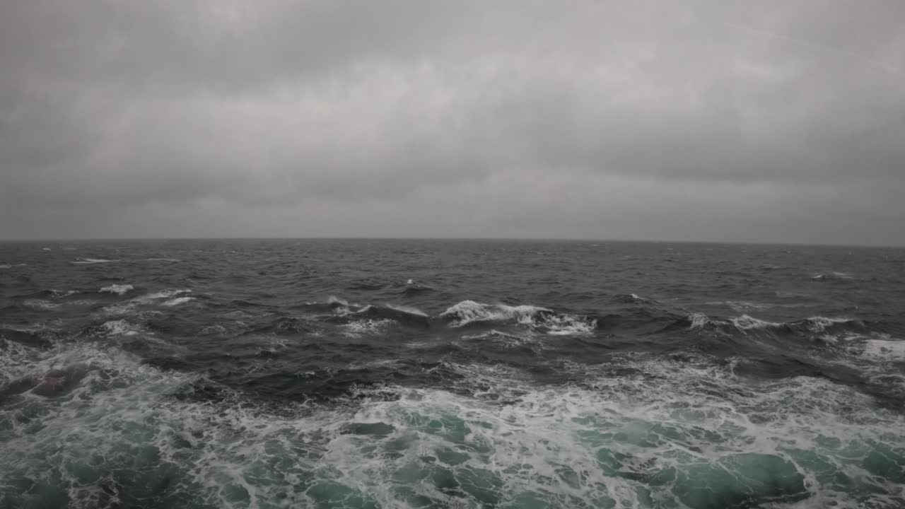 Dark waves crash across a fjord near Flåm, Norway, as thick clouds obscure the horizon, capturing the raw power and moodiness of Nordic waters in stormy weather