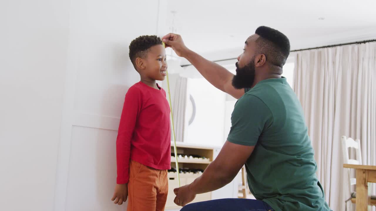 Happy african american father and son measuring height, in slow motion