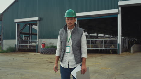 livestock supervisor making notes holding clipboard at modern cowshed building.