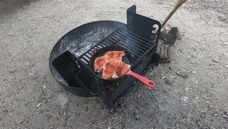 cocinar salmón rojo en una sartén de hierro fundido rojo sobre una fogata mientras atiende el fuego