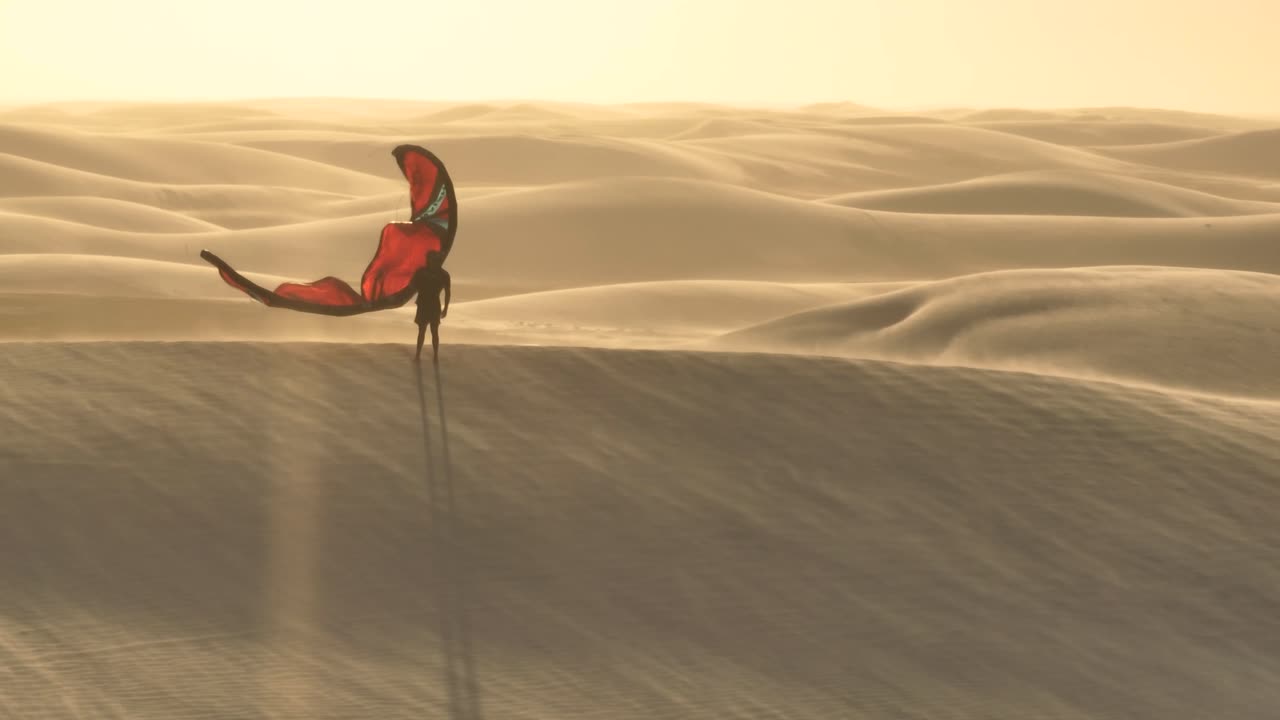 강한 바람과 낮은 따뜻한 태양이 긴 그림자를 드리우면서 모래 언덕 꼭대기에 서 있는 한 사람의 극적인 항공 샷