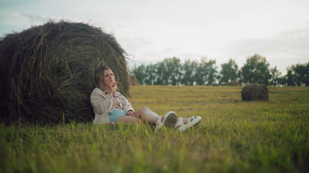 바닥에 앉아, 다리를 고, 은 시골 에서 쳐진 잎자루에 기대어 앉아있는 사려 깊은 여성, 상으로 손을 들고, 조용한 분위기, 어져있는 풀