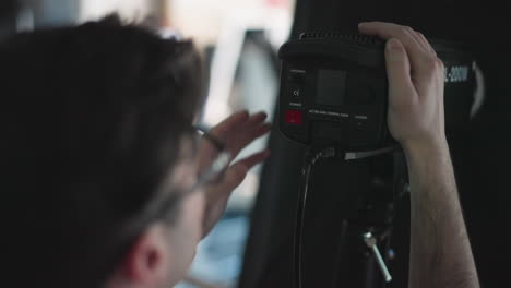 camera technician pressing power switch on led panel to adjust studio light settings during broadcast filming session cables and mounting hardware visible blue background production environment