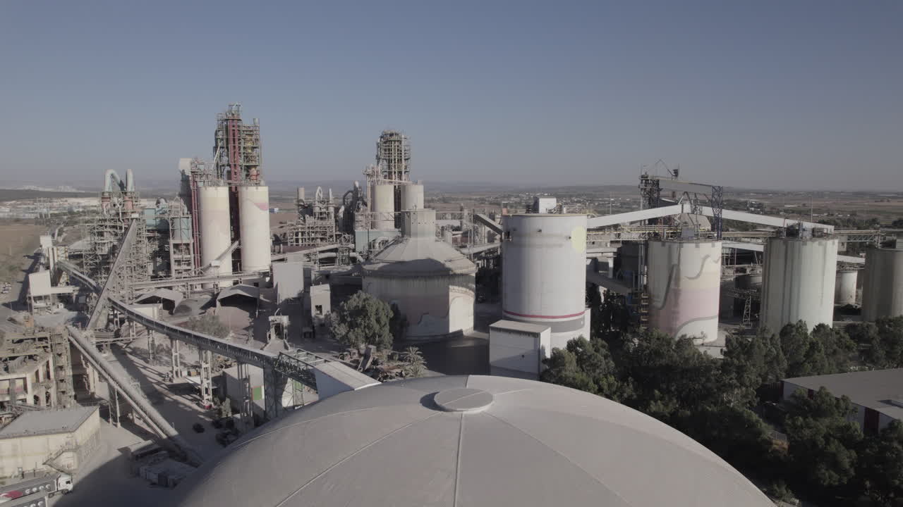 Aerial shot of a huge cement factory, innovative industrial area with lots of hangars and trucks, beautiful area with trees, parallax shot