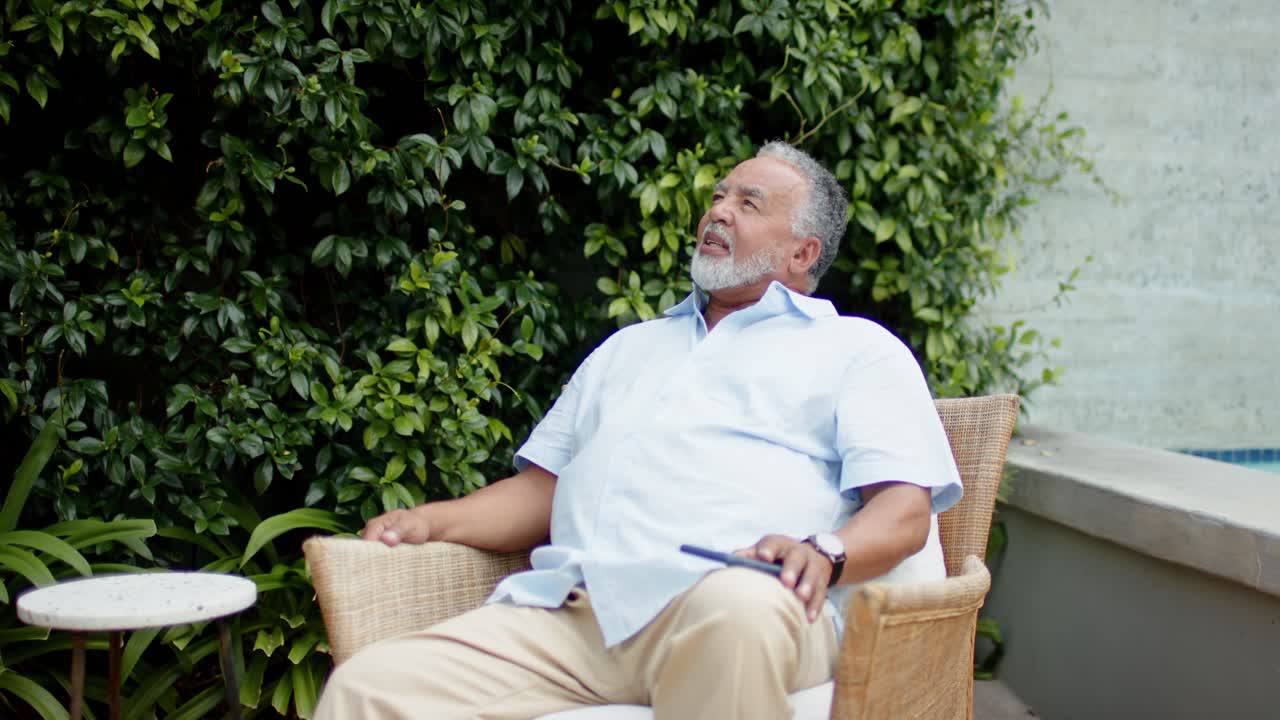 Hombre afroamericano mayor moviéndose, levantando la cabeza, escudriñando el seto en el jardín sosteniendo curiosamente un control remoto