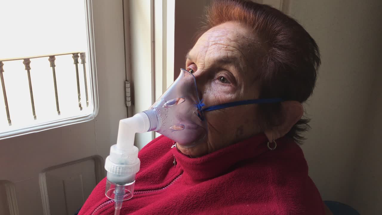 plano medio de una anciana caucásica inhalando medicamentos de un nebulizador en casa
