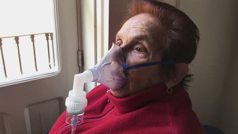 medium shot of an elderly caucasian woman inhaling medication from a nebulizer at home