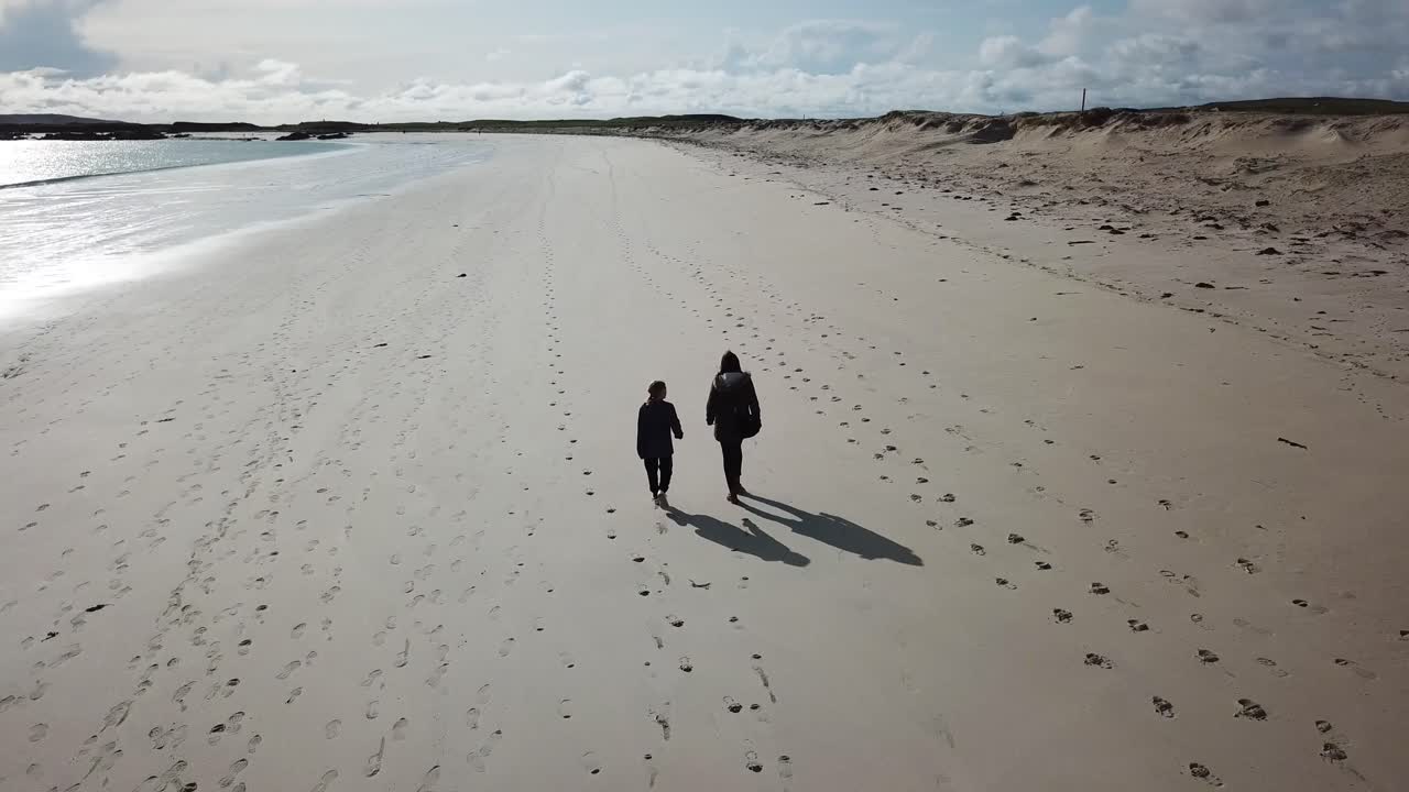 Najazd kamery z lotu ptaka: dwie osoby idą po dużej piaszczystej plaży w Connemarze w Irlandii